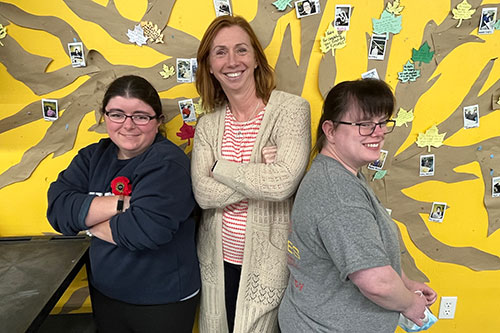 three women standing against a bright yellow wall