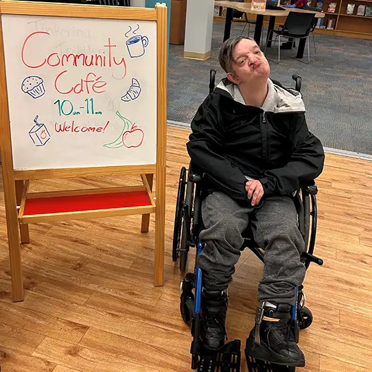 man in wheelchair next to community cafe sign