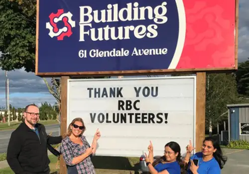 group of RBC volunteers pointing at Building Futures sign